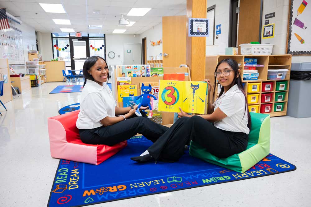 Two students sitting on a carpet in a childhood education class.