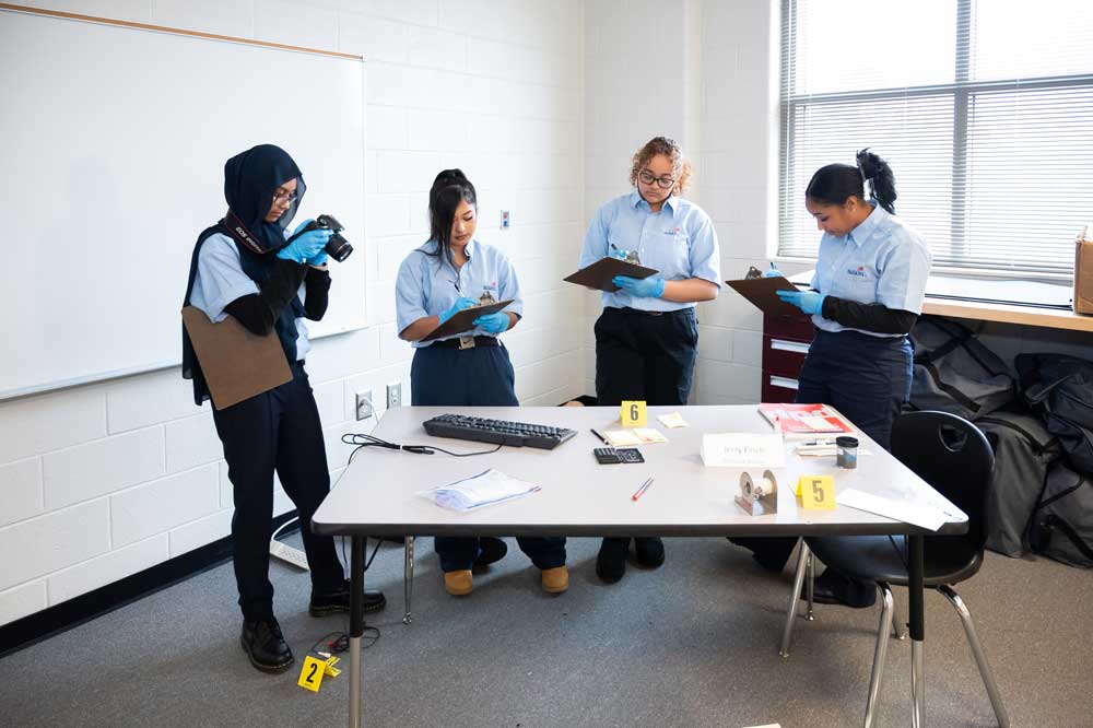 Four crime scene investigation students observing a crime scene set up.