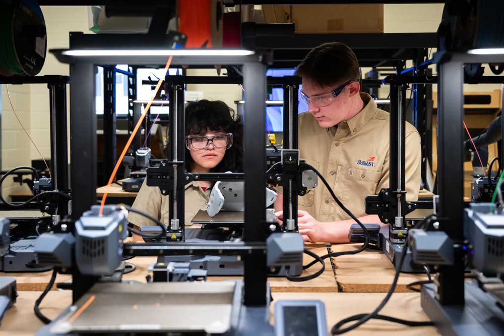 Two manufacturing students work at a machine. 